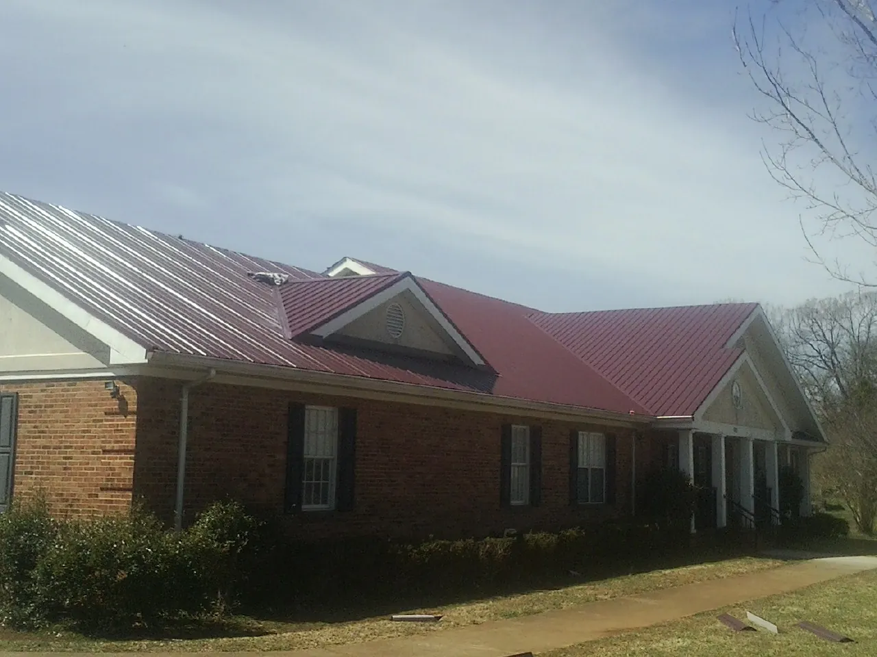 Red metal roof with gabled entries on a long brick building, from a Hail Damage Roof Repair job in Statham