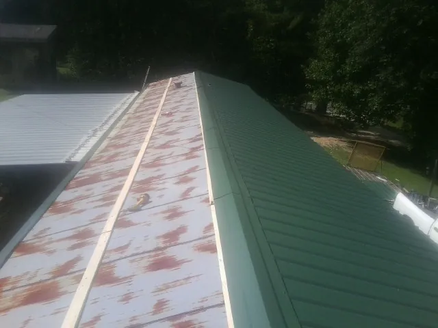Old rusted panels beside newly installed green metal roofing — Wind Damage Roof Repair by Roofing Brothers in Statham