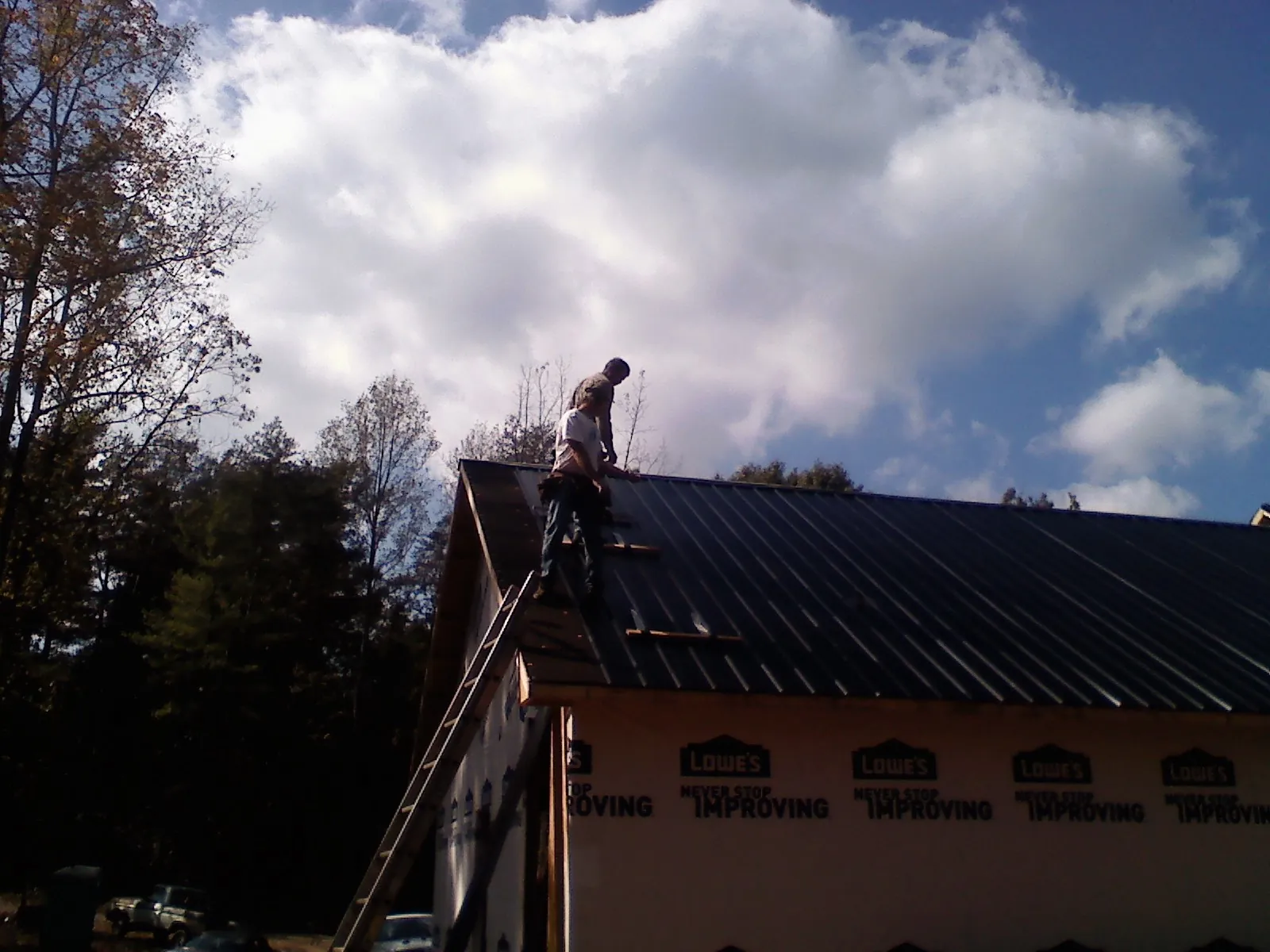 Roofer fastening dark metal panels high against a cloudy sky, from a Roof Inspection job in Statham