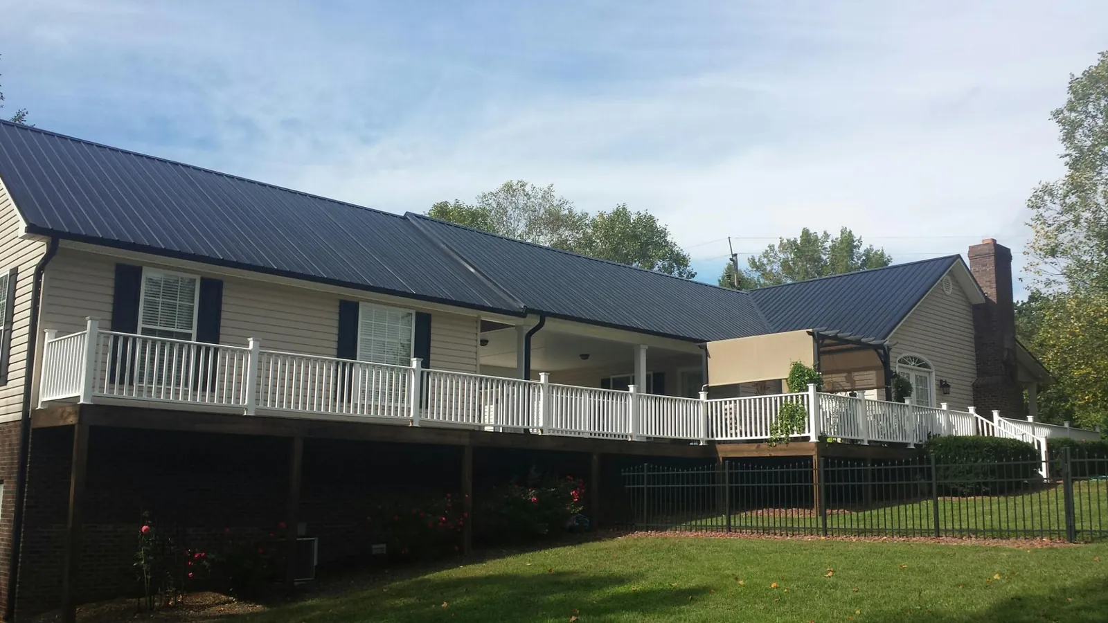 Black metal roof above a long white railed deck on a hillside home in Statham