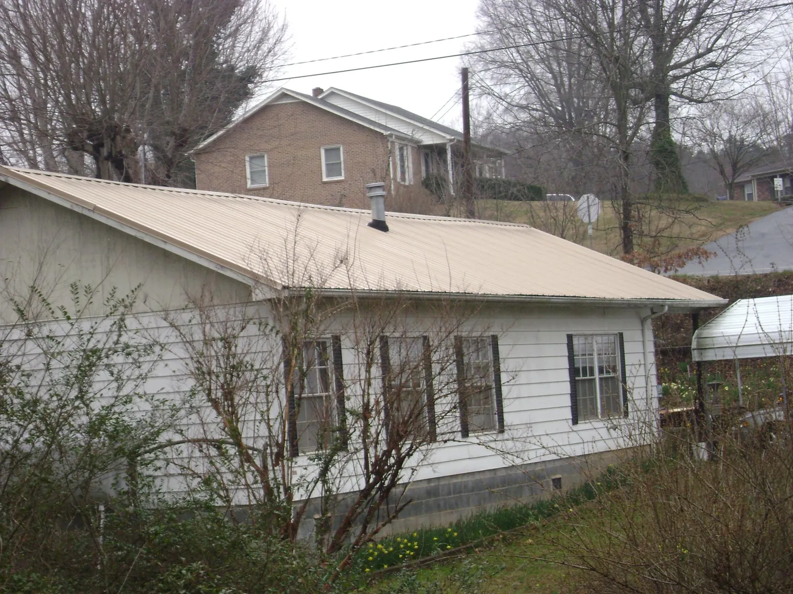 Tan metal roof on a white sided house set into a hillside — Commercial Roofing by Roofing Brothers in Statham